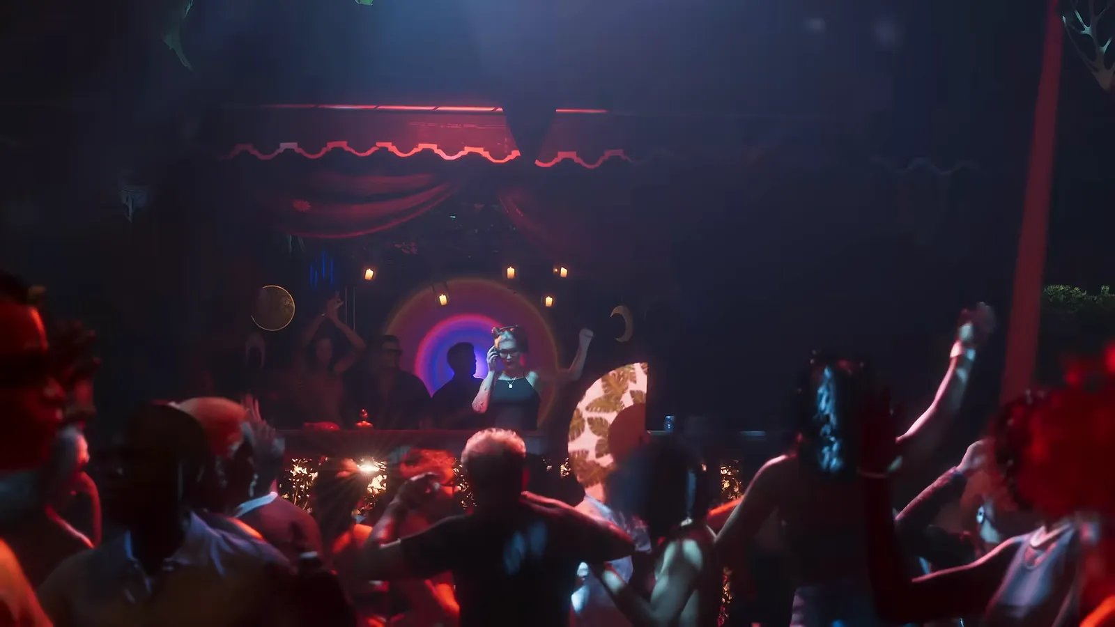 Club Space in GTA VI: Clubbers dance in front of a DJ booth under red lights and hanging greenery.