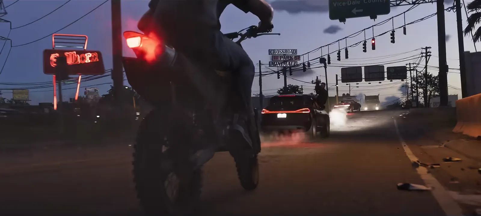 Port Gellhorn in GTA VI: Dusk on a Port Gellhorn highway strip: the Gellhorn roadhouse neon, a Crossroad Park minimall sign and traffic signals.